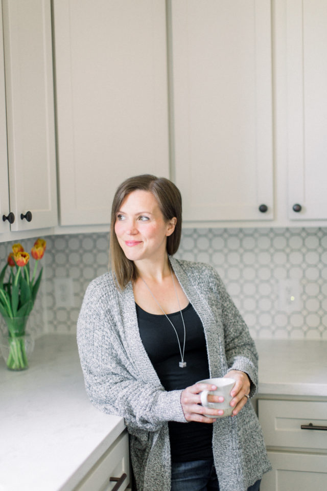 Blog creator, Erin Jensen, holding a white mug and standing in a kitchen.