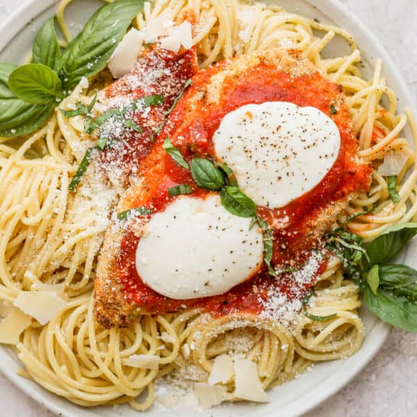 A plate of spaghetti noodles and a piece of baked chicken parmesan.