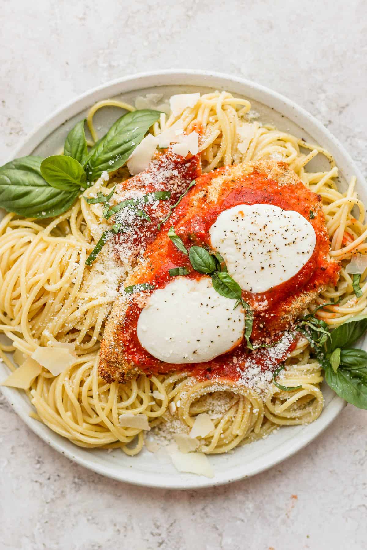 Baked chicken parmesan with noodles and basil on a plate.