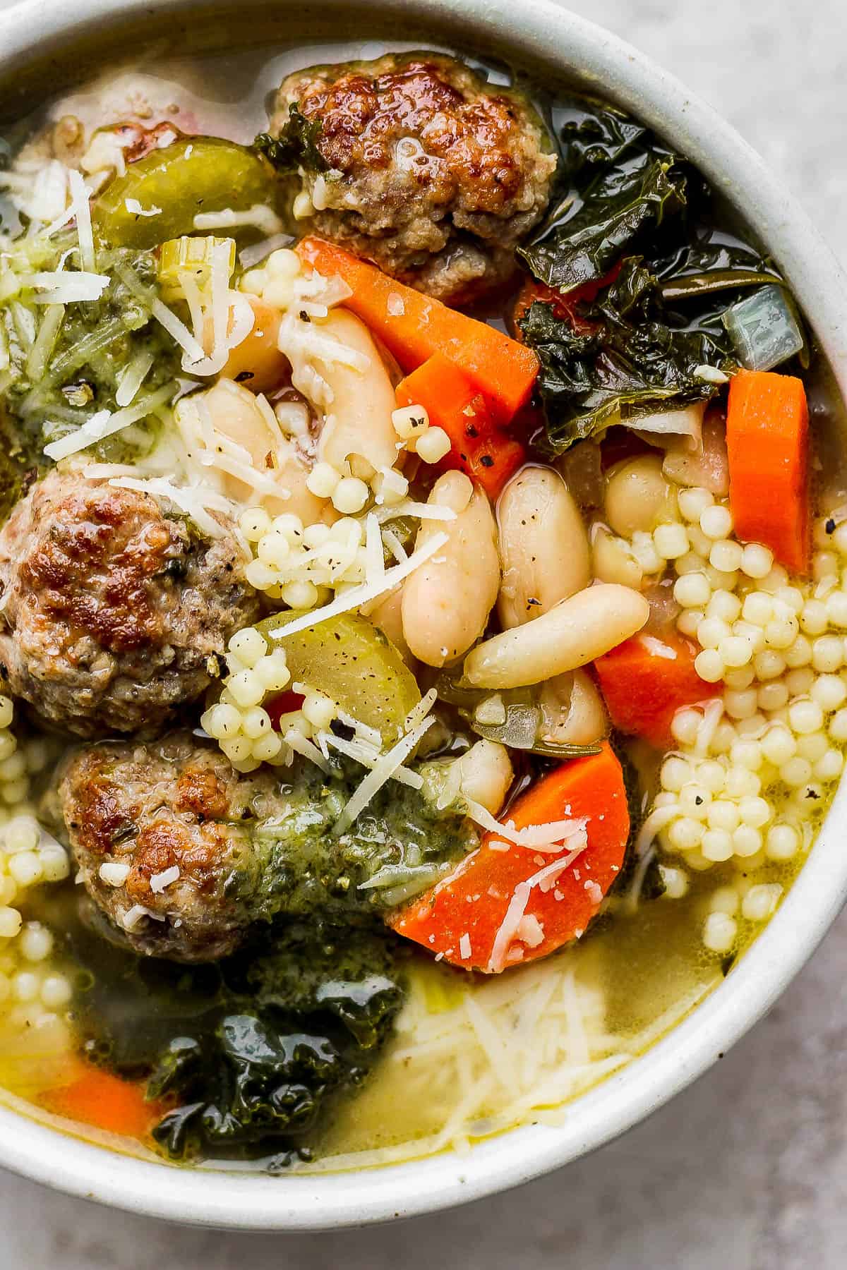 A bowl of Italian wedding soup with basil pesto and parmesan cheese on top.