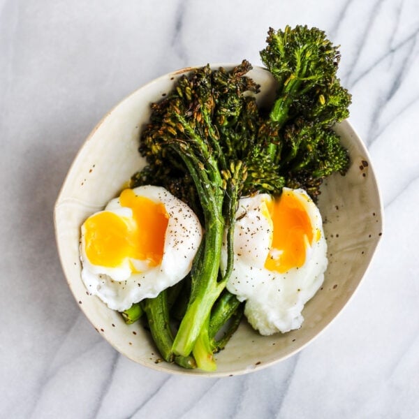 Roasted broccolini in a bowl with two poached eggs.
