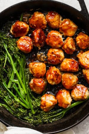 Cast iron skillet filled with teriyaki chicken meatballs and broccolini.
