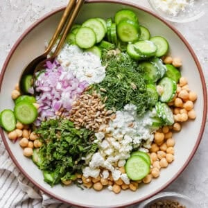 A bowl of Cucumber Chickpea Salad with sunflower seeds, feta and herbs with a spoon sticking out.