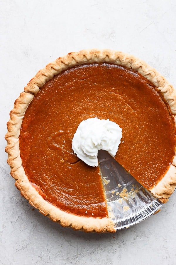 Delicious Dairy-Free Pumpkin Pie - a perfectly delicious Thanksgiving pumpkin pie with no dairy added! #dairyfreepumpkinpie #dairyfreepumpkinpierecipe #pumpkinpiedairyfree #pumpkinpierecipe Dairy free pumpkin pie with whipped coconut cream in the center and a piece cut out.
