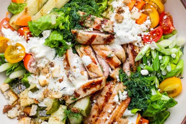 Grilled chicken thighs on top of a dill pickle chicken salad with dressing.