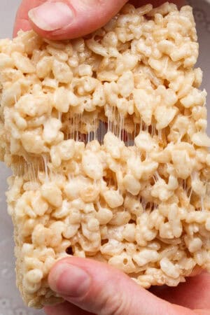 Someone holding an extra gooey rice krispie treat and pulling it apart.