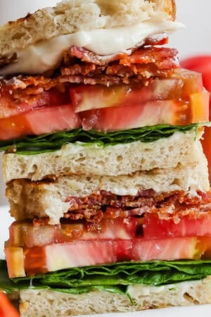 A stacked grilled blt on a plate with tomatoes next to it.