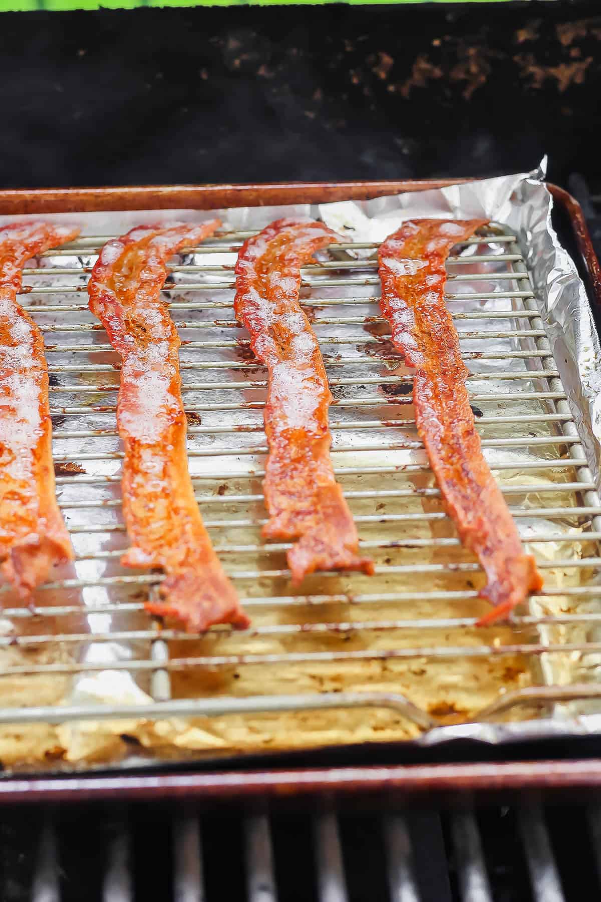 A rimmed baking sheet lined with foil with a wire rack on top with cooked bacon laying on top of the wire rack.