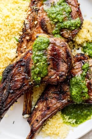 A plate of three grilled lamb chops on a plate with some mint chimichurri on top and some lemon couscous underneath it.