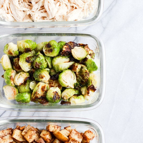 Meal prep containers lined up next to each other, one has shredded chicken, one has cooked brussel sprouts, and one has cooked potatoes.