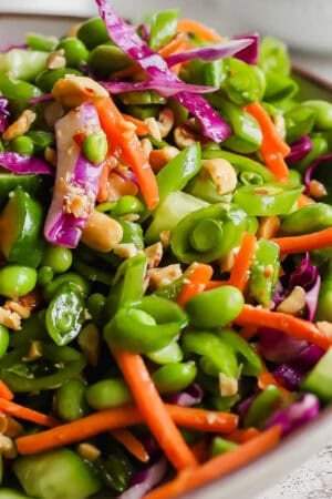 A bowl filled with a chopped pea salad with carrots, edamame, cabbage and chopped peanuts.