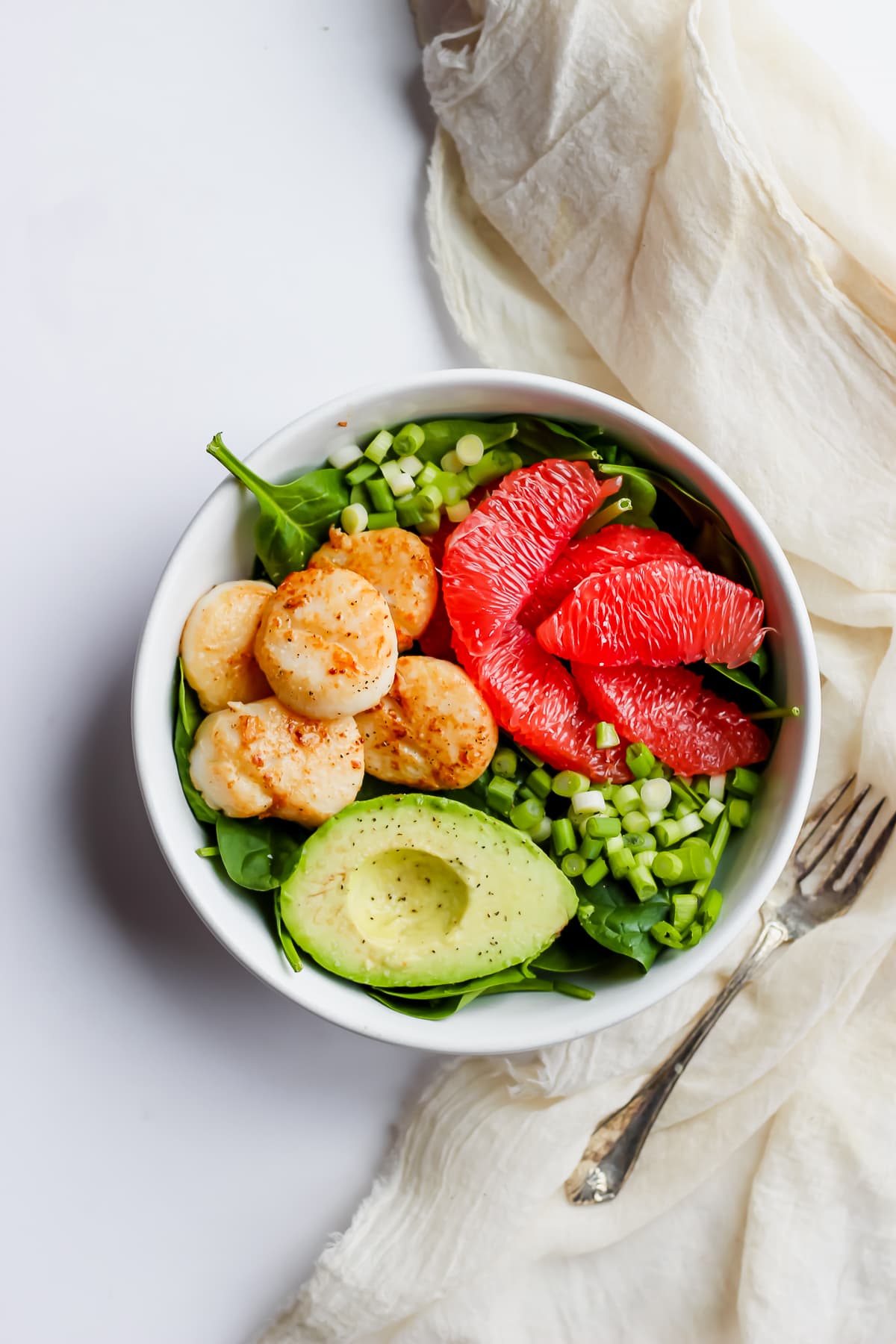A seared scallop salad with grapefruit and avocado with a fork next to it.