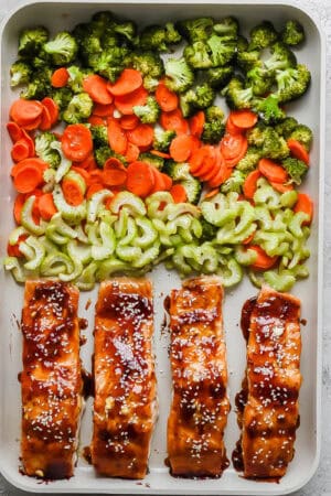 A sheet pan full of four salmon fillets, celery, carrots, and broccoli.