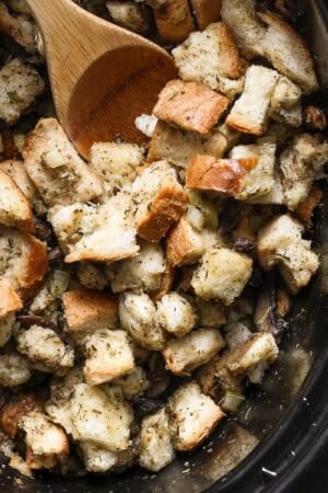 Top down shot of a slow cooker filled with stuffing and a wooden spoon sticking out.