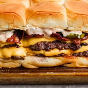 Smash burger sliders on a baking sheet with burger sauce, melted cheese, bacon and pickles.