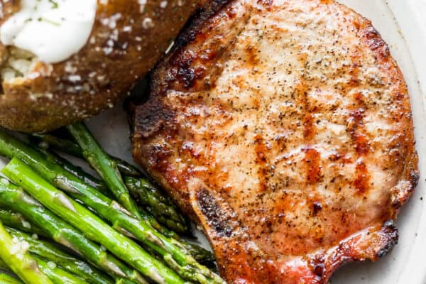 A plate with a smoked pork chop, baked potato and smoked asparagus.