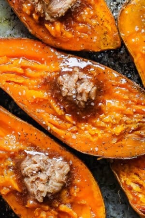 Halved smoked sweet potatoes on a baking sheet with cinnamon sugar butter on top.