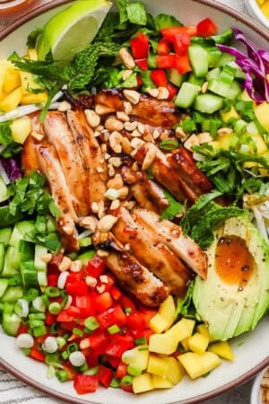 A bowl of chicken spring roll salad with avocado, red pepper, mango and sweet chili sauce with crushed peanuts.