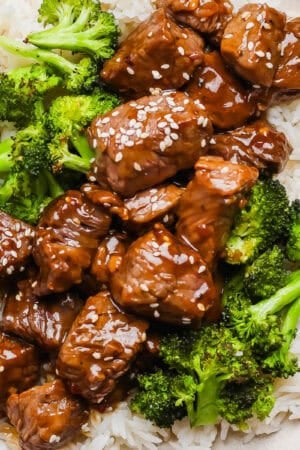 A plate of rice with roasted broccoli and teriyaki steak bites on top with sesame seeds.