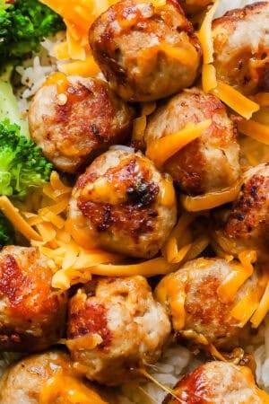 A plate with rice, broccoli and turkey cheddar meatballs with shredded cheddar cheese around the meatballs.