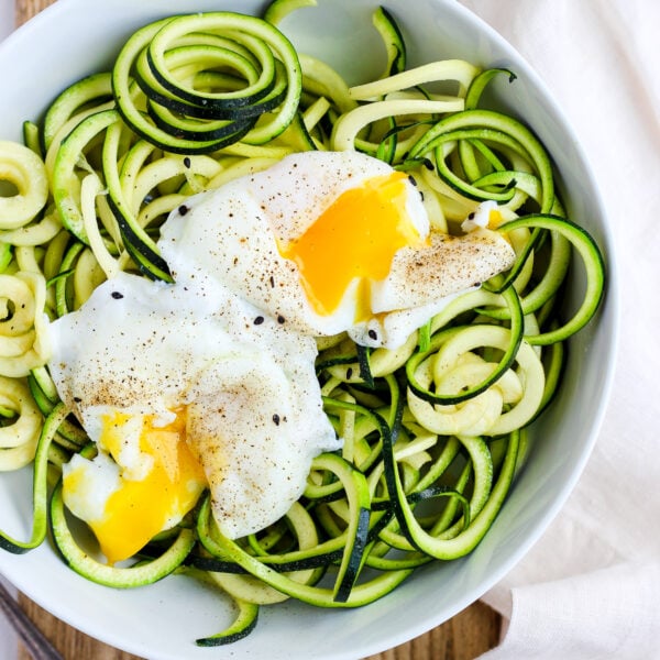 A bowl of zoodles with two poached eggs on top and sprinkled with black pepper.
